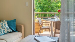 A balcony with a table set for dining, a sofa with patterned cushions, and a view of greenery outside. - Byron BaySide Central Studio Apartments (Byron Bay)