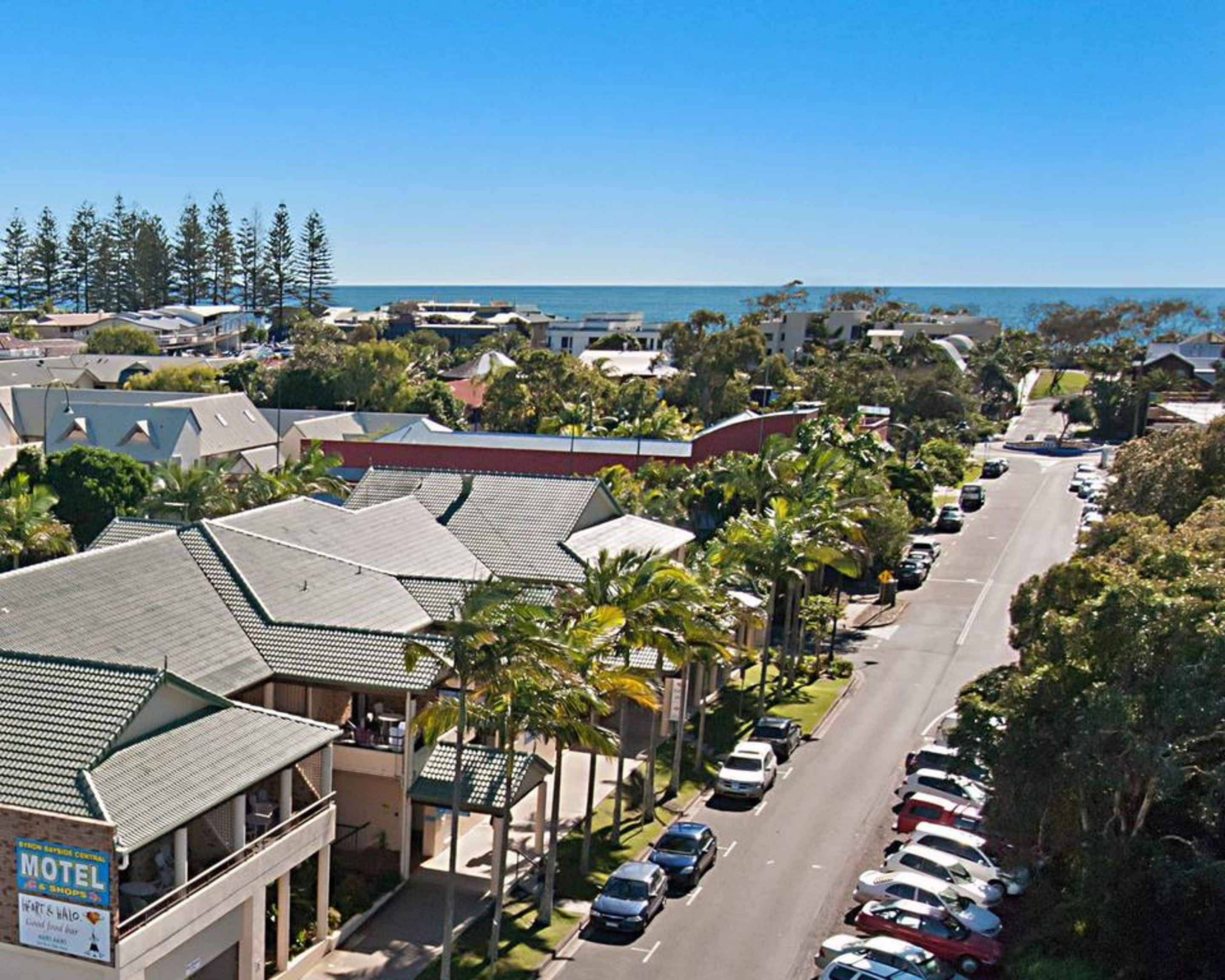A coastal motel with multiple-story buildings, a parking lot, and a view of the ocean.