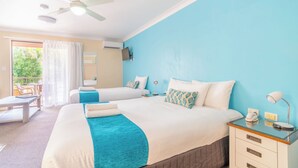 A hotel room with two beds, a ceiling fan, a TV, and a balcony with a table and chairs. - Byron BaySide Central Studio Apartments (Byron Bay)
