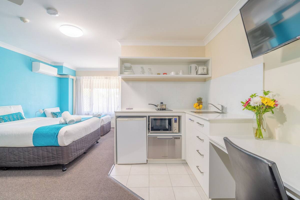 Una habitación de hotel compacta con una cama, kitchenette, TV de pantalla plana y baño pequeño.