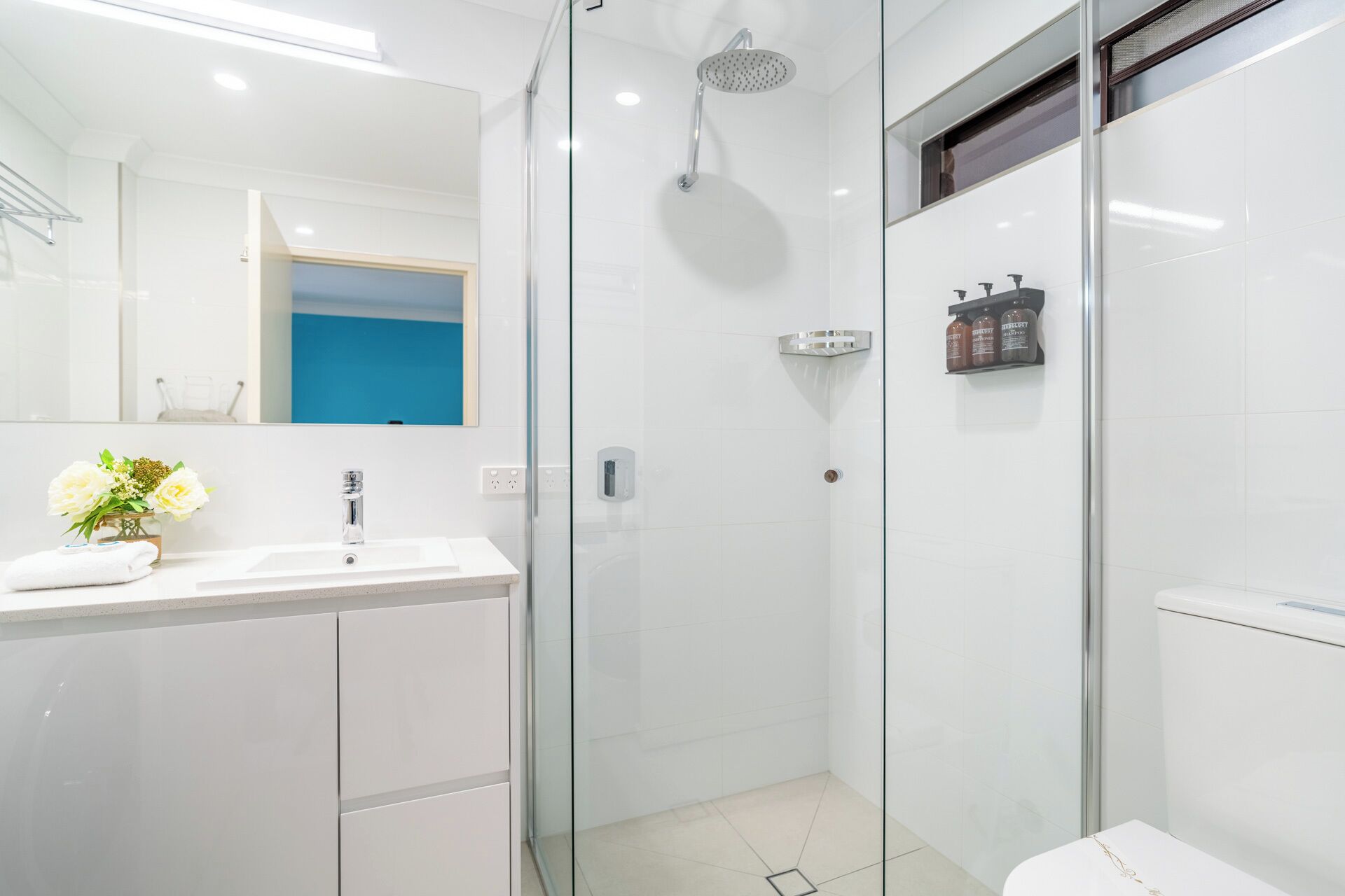A modern bathroom with a glass shower enclosure, a white sink, and a mirror.