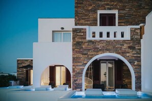 A modern building with stone and white facades, a swimming pool, and outdoor seating areas. - Aegean Land (Naxos)
