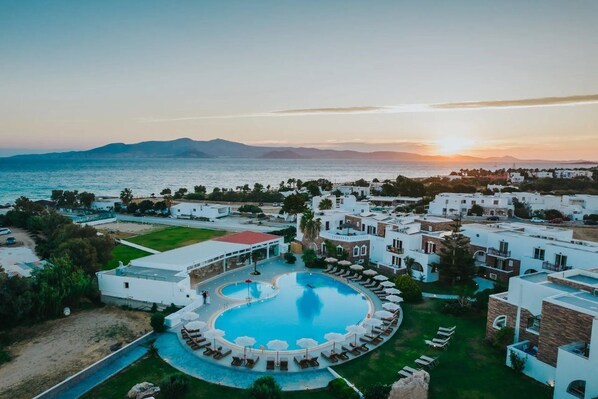 A resort with a swimming pool, white buildings, and a view of the sea at sunset. - Aegean Land (Naxos)