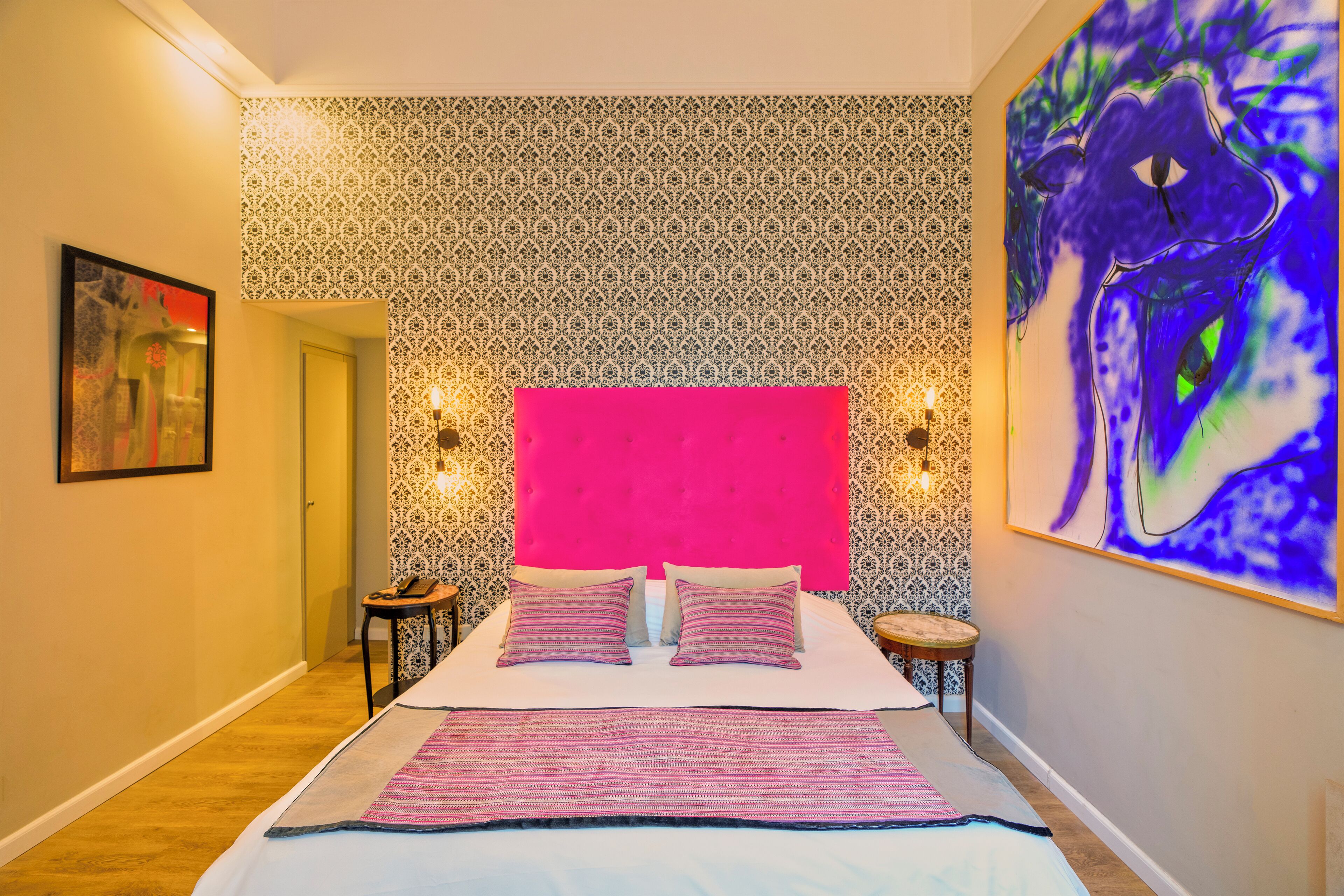 Une chambre à coucher avec un papier peint à motifs, une tête de lit rose et un lit avec une literie à rayures.