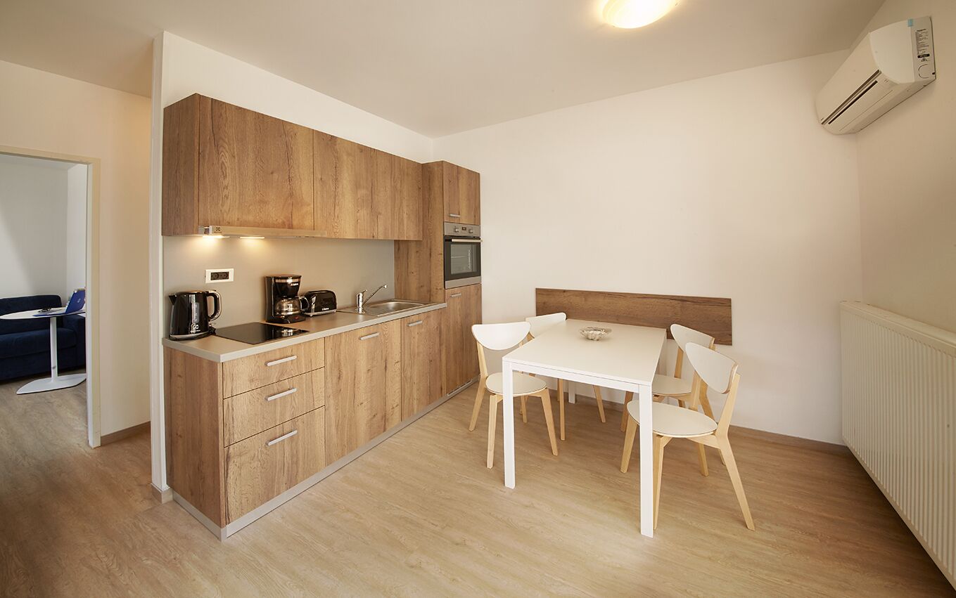 A compact kitchen with wooden cabinets, a built-in oven, and a dining area with a white table and chairs.