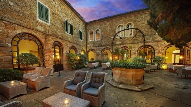A courtyard with stone walls, arched doorways, wicker furniture, and potted plants.