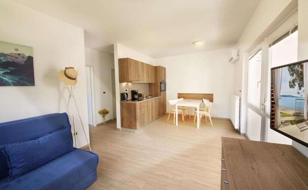 A modern living room with a blue sofa, a wooden dining table, and a kitchen area with wooden cabinets and a white countertop.