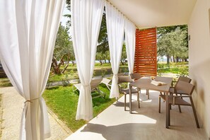Un espace extérieur aménagé, abrité et doté de tables et de chaises, offrant une vue sur un paysage verdoyant avec des arbres et une étendue d’eau.