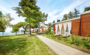 Une rangée de cabanes en bois avec des rideaux blancs, un chemin pavé et une vue sur la mer.