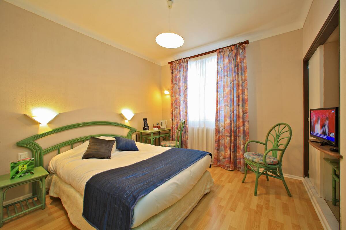 A hotel room with a bed, a television, a chair, and a small table with a lamp.