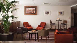 A modern living room with a flat-screen TV mounted on the wall, a potted plant, and a variety of seating options including armchairs and a sofa. - Leonardo Hotel Bradford (Bradford)