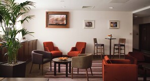 A modern living room with a flat-screen TV mounted on the wall, a potted plant, and a variety of seating options including armchairs and a sofa. - Leonardo Hotel Bradford (Bradford)