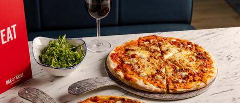 A pizza with a glass of red wine and a bowl of greens on a table.