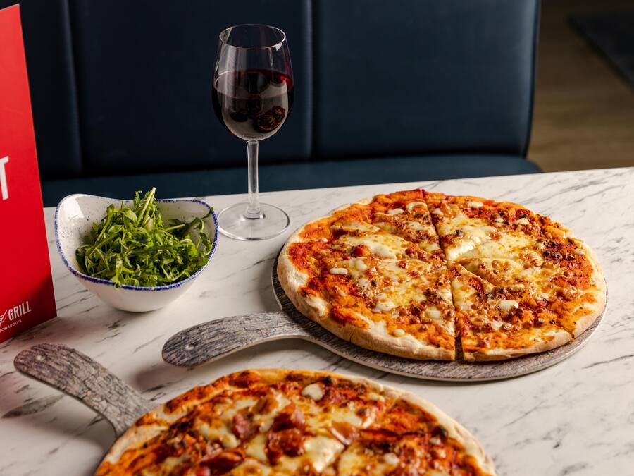 Uma pizza com um copo de vinho tinto e uma saladeira sobre a mesa.