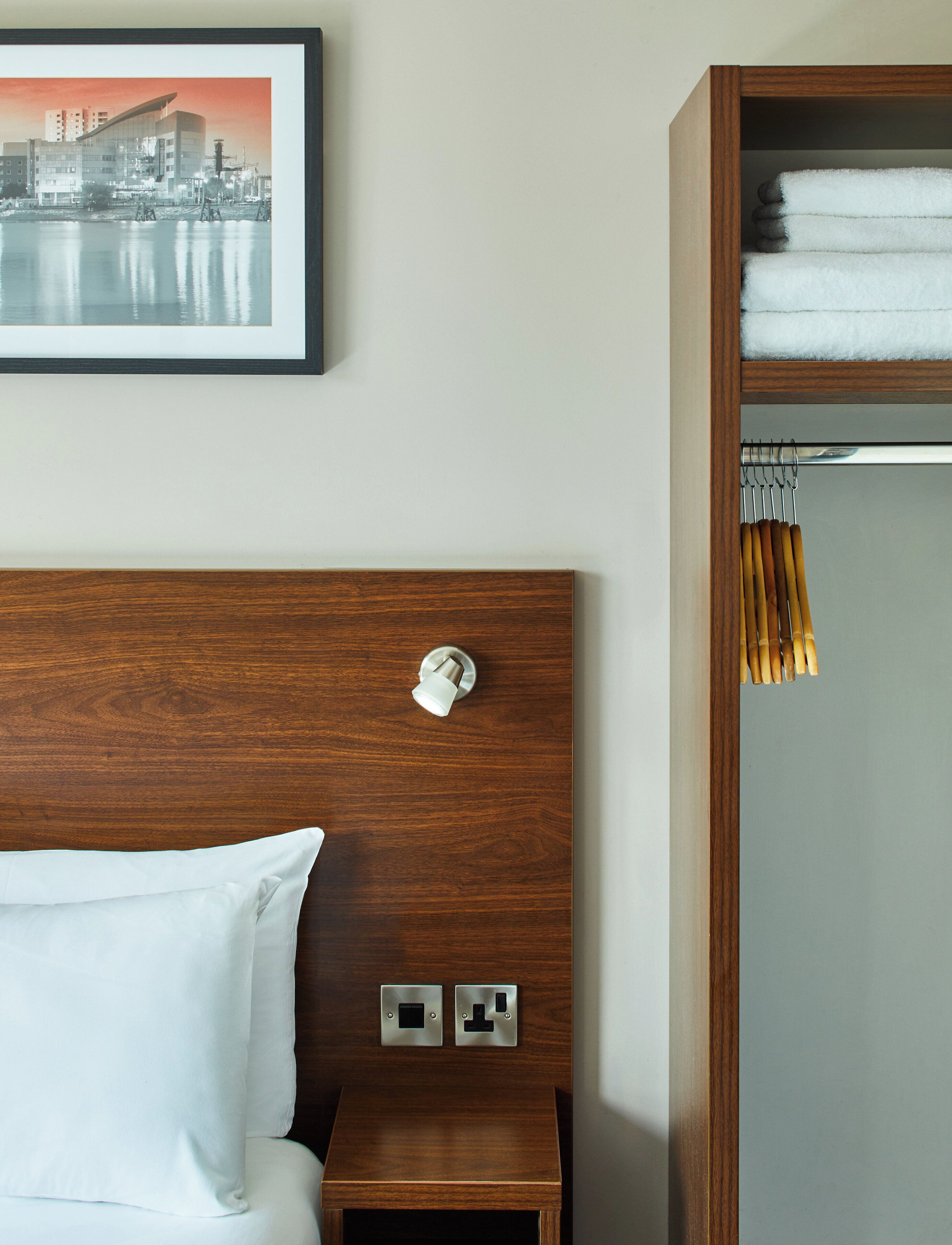 A hotel room with a wooden headboard, a bed with white linens, a nightstand with two switches, and a framed picture on the wall.