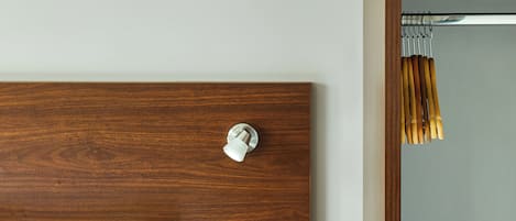 Una habitación de hotel con cabecera de madera, cama con ropa de cama blanca, mesita de noche con dos interruptores y un cuadro enmarcado en la pared.