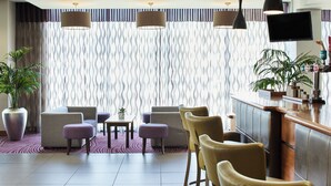 A modern hotel lobby with seating arrangements, a bar area, and a large window with patterned curtains. - Leonardo Hotel Bradford (Bradford)