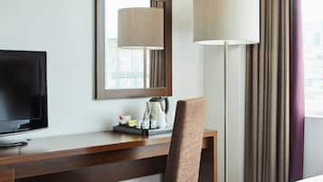 Une chambre d’hôtel avec un bureau en bois, une télévision, un miroir, une lampe et une chaise.