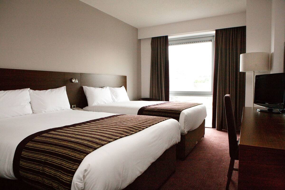 A hotel room with two beds, a desk with a computer, and a window with curtains.