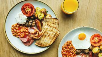 Une assiette de petit-déjeuner avec des œufs, du bacon, des haricots, des champignons, des tomates et des toasts, posée sur une table en bois.