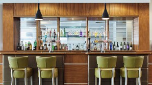 A bar area with wooden paneling, multiple liquor bottles, and green bar stools. - Leonardo Hotel Bradford (Bradford)