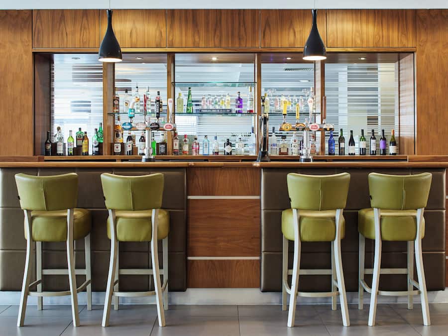 A bar area with a wooden counter, multiple liquor bottles, and four green bar stools.