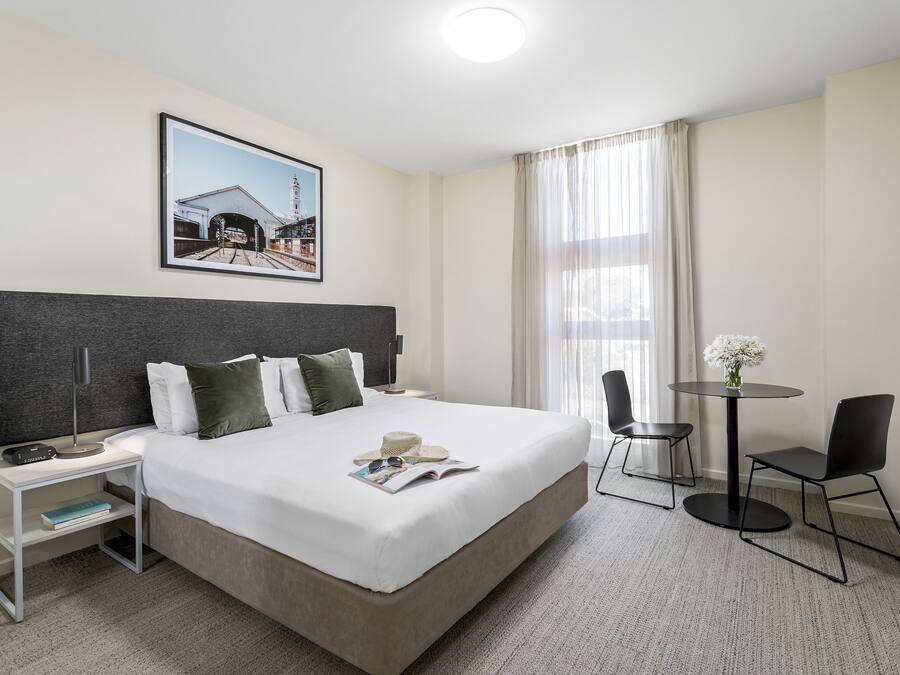 Ein Hotelzimmer mit einem großen Bett, Nachttisch, Lampe und einem kleinen Tisch mit Stühlen.