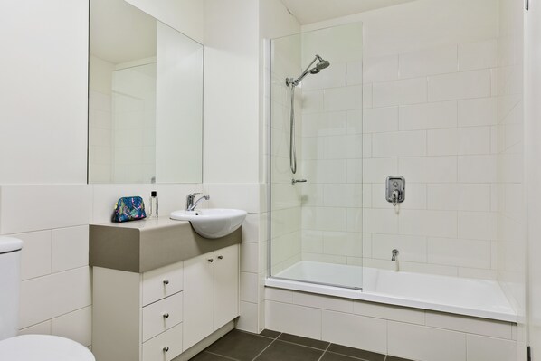 Un baño moderno con ducha de vidrio, lavamanos blanco y retrete.