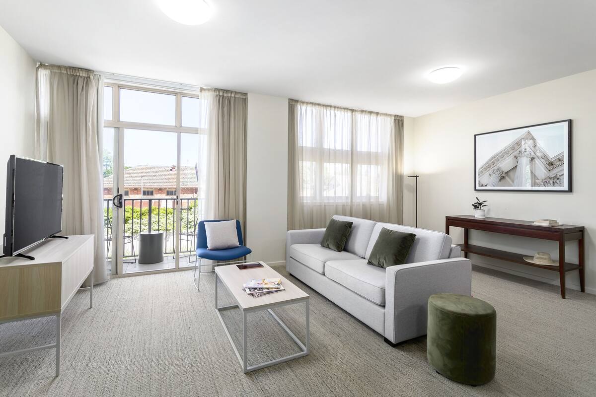 Una sala de estar moderna con sofá, mesa de centro, televisor y vistas al exterior.