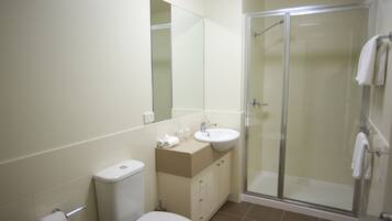 Een badkamer met toilet, wastafel, spiegel en een douche met glazen wanden.