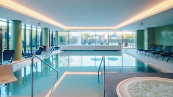 Una piscina interior moderna con paredes de vidrio transparente, sillas de descanso y zona de hidromasaje.