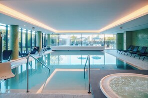 Een modern binnenzwembad met glazen wanden, lounge fauteuils en een whirlpool.
