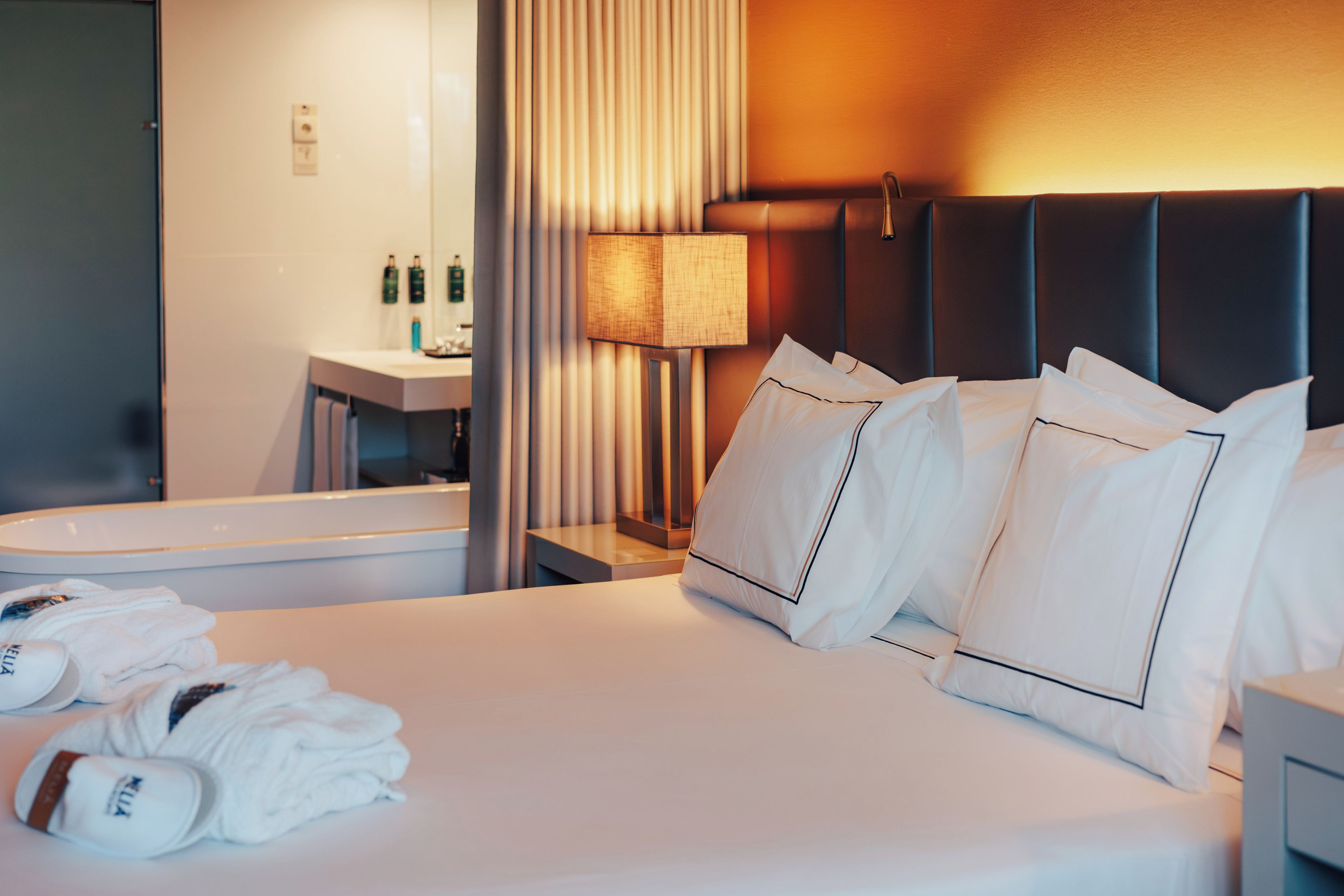 Une chambre d’hôtel comprenant un lit, des oreillers, une table de chevet, une lampe, ainsi qu’une salle de bain avec un lavabo et des articles de toilette.