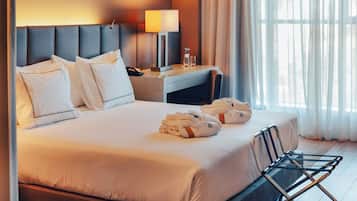 A hotel room with a large bed, a desk with a lamp, a chair, and a window with curtains.