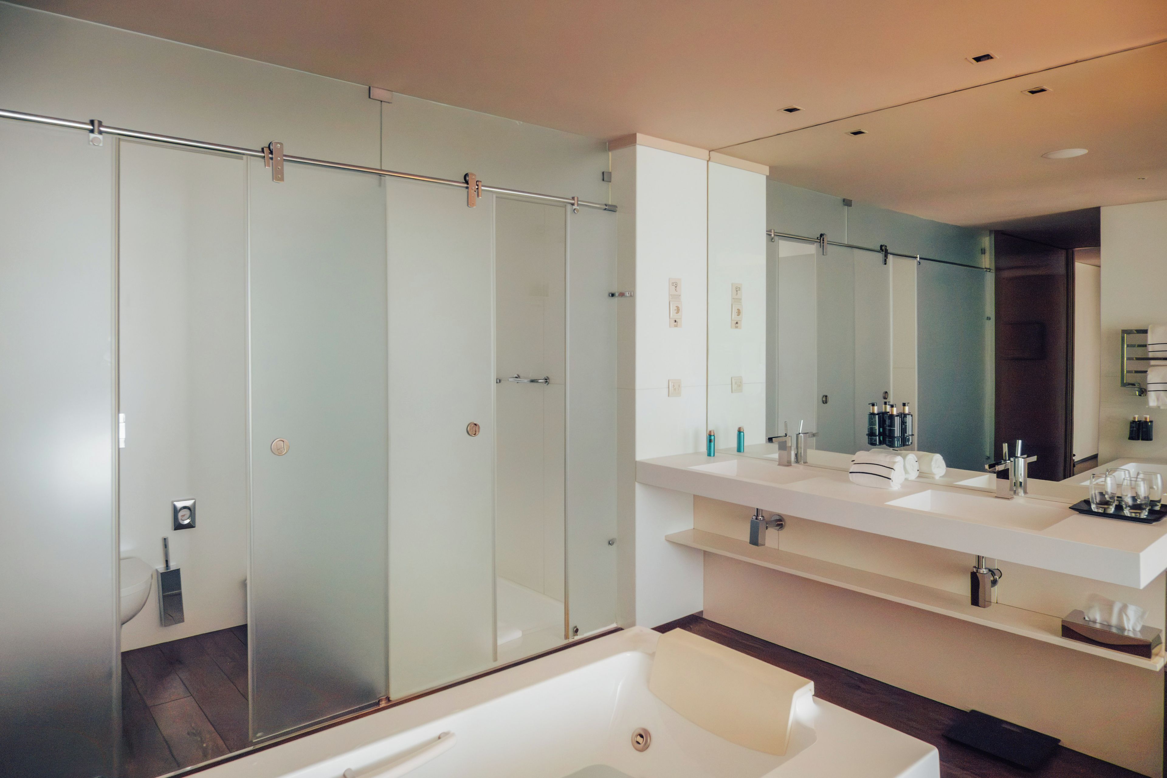 A modern bathroom with a glass-enclosed shower, a large mirror, and a white bathtub.