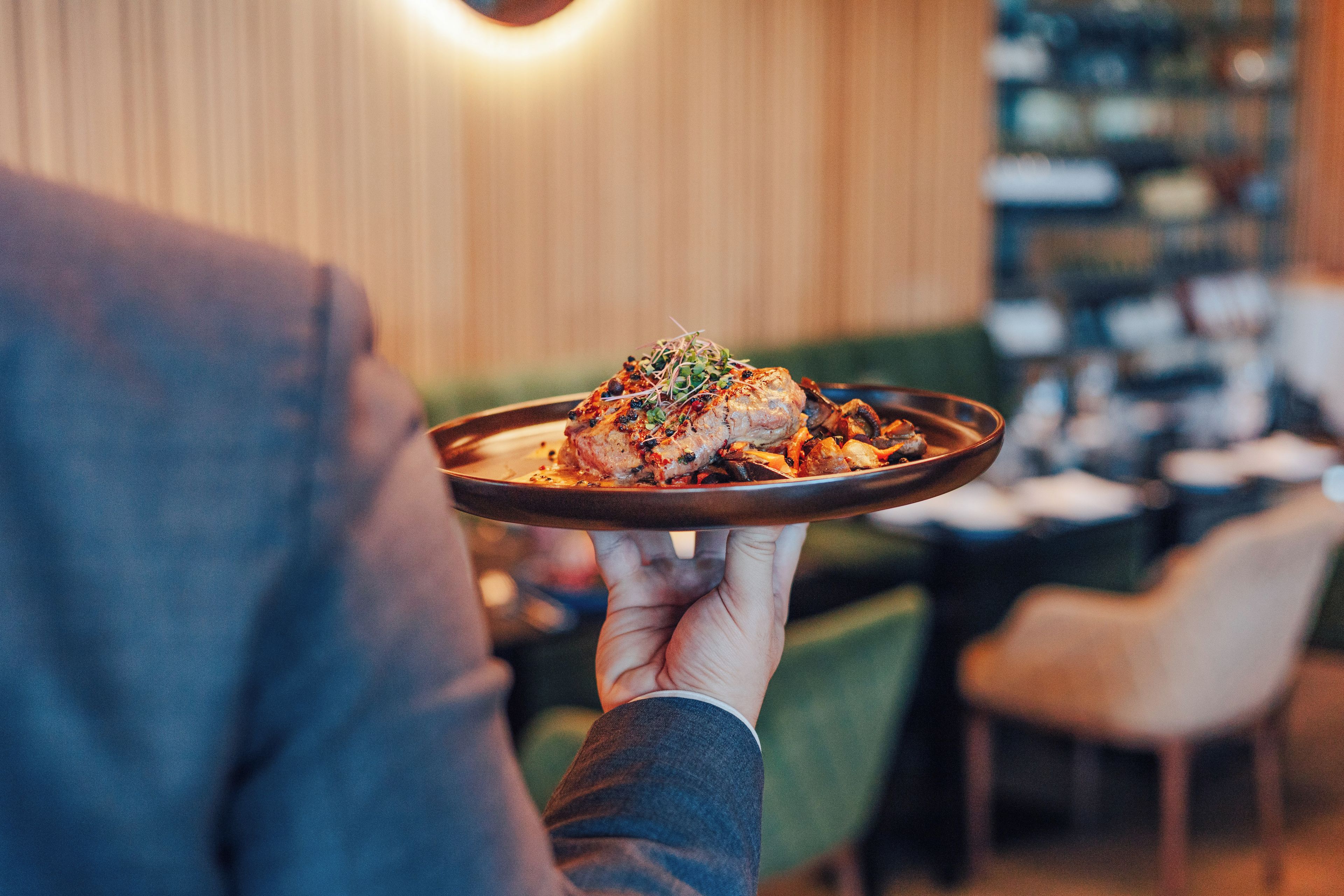 A person holding a plate with food, in a restaurant with tables and chairs.