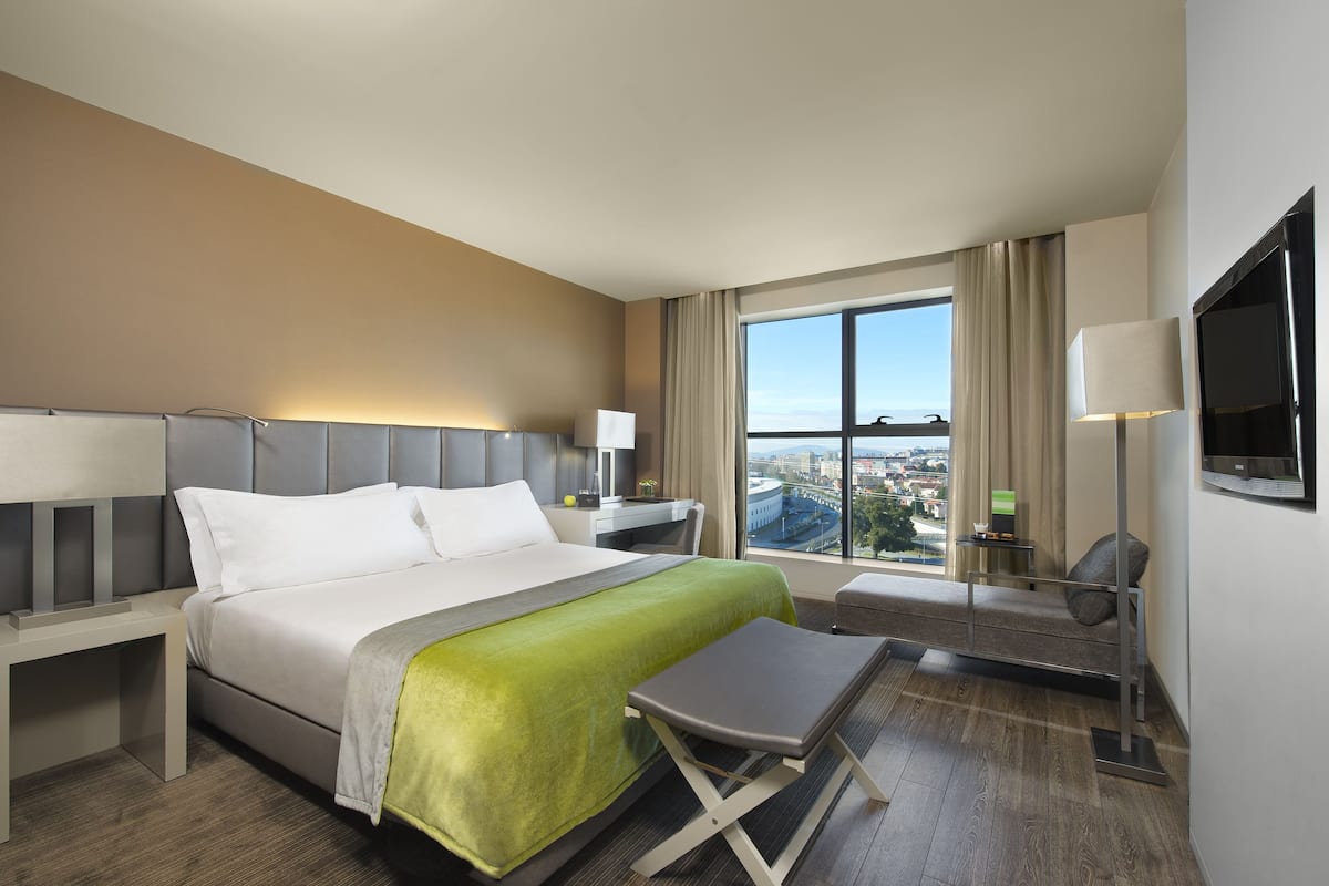 Een moderne hotelkamer met een groot bed, een bureau, een stoel, een televisie en uitzicht op de stad.