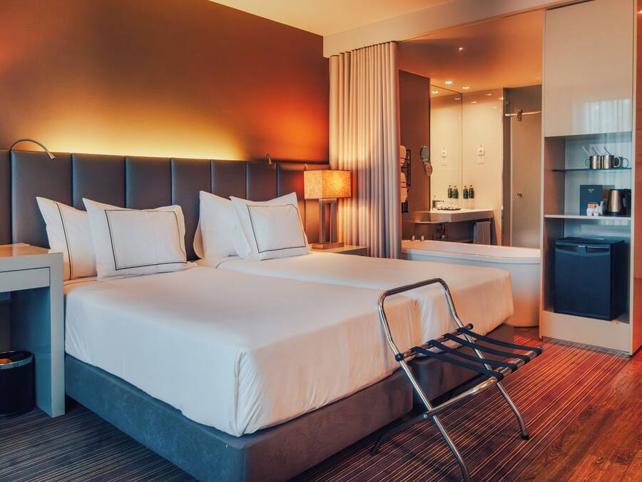 Una habitación de hotel con una cama grande, mesitas de noche, un escritorio, una silla, un espejo y una kitchenette.