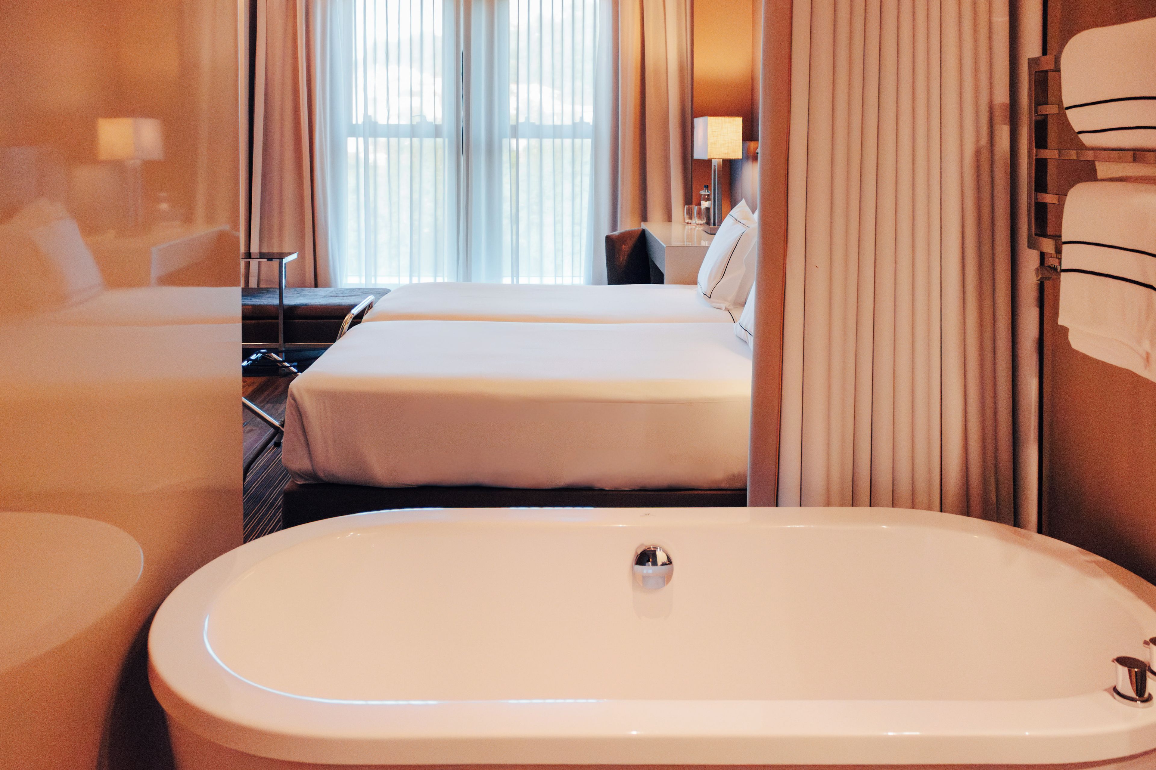 Een hotelkamer met een groot bad, een tweepersoonsbed en een bureau met een stoel.