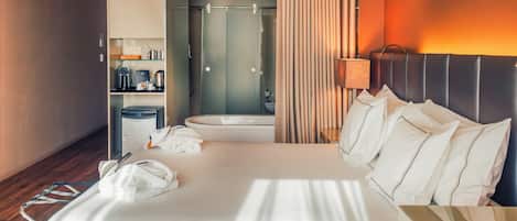 Una habitación de hotel con una cama grande, un baño con ducha y una nevera pequeña.
