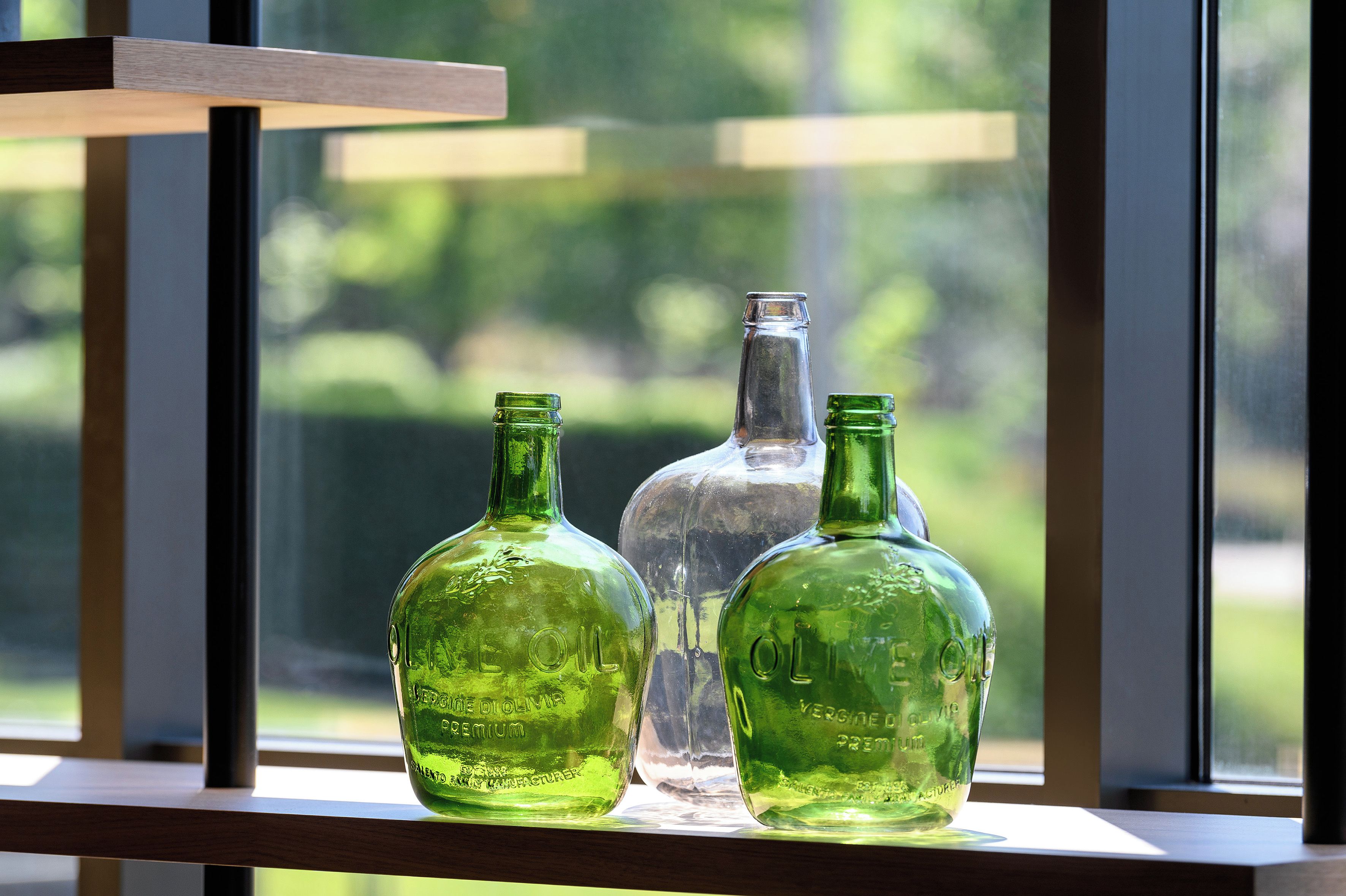 Drei Glasflaschen auf einem Regal neben einem Fenster, unscharfer grüner Hintergrund.