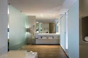 Une salle de bain moderne avec un plancher en bois, un grand miroir, un lavabo blanc et une cloison en verre.