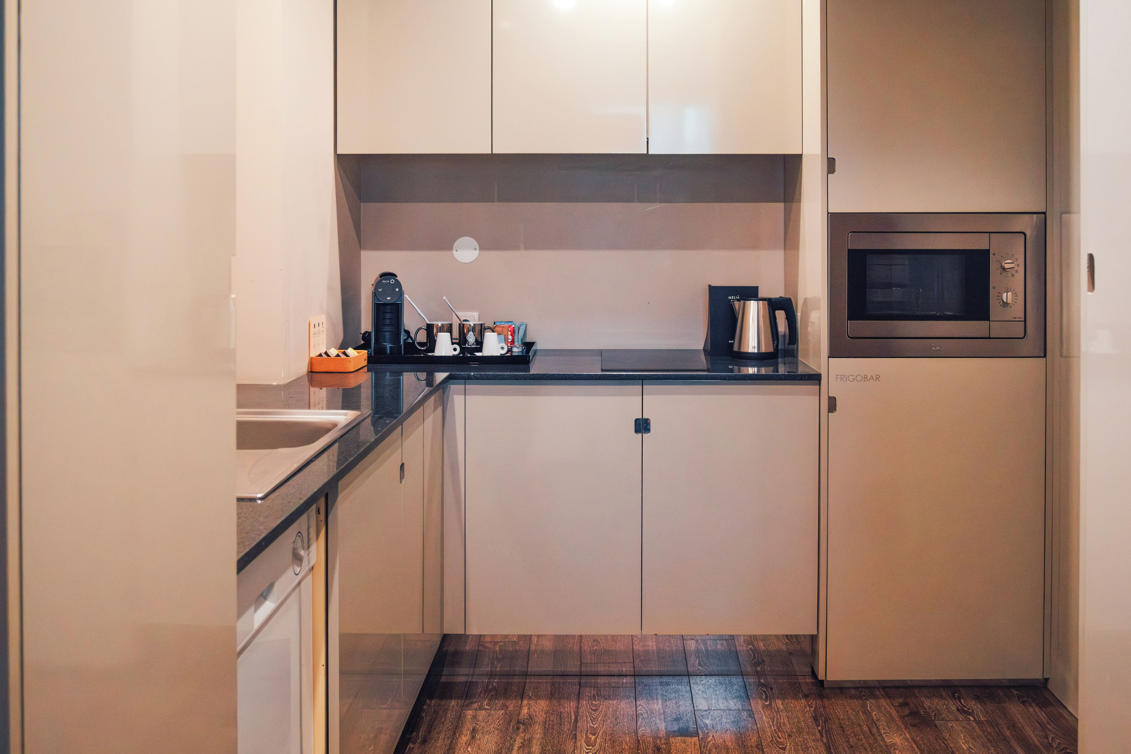 Una cocina compacta con microondas, cafetera y un lavamanos pequeño.
