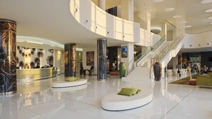Un hall d’entrée spacieux avec un escalier central, un comptoir d’accueil et des espaces de détente modernes.