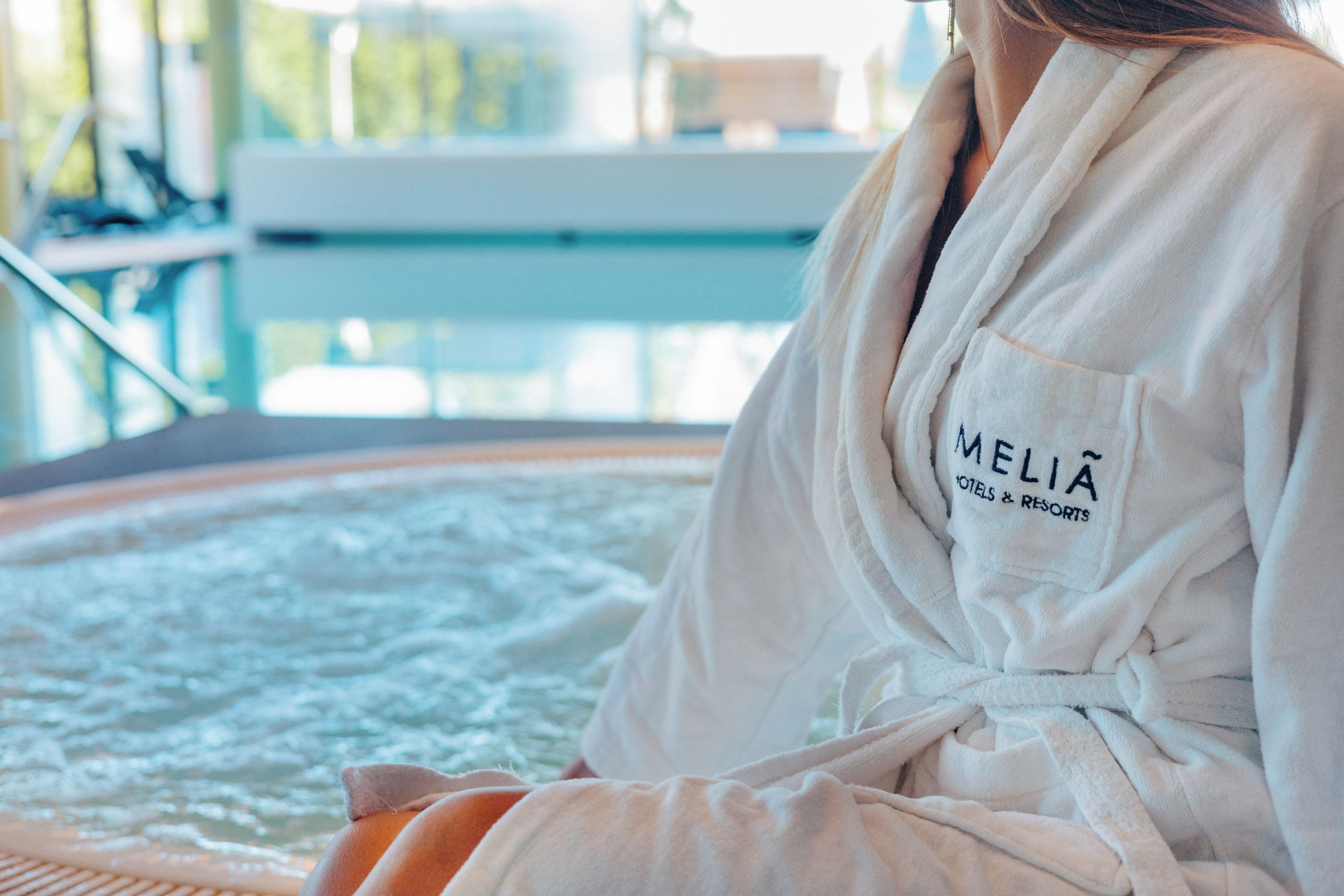 A person sitting in a bathtub with a towel, wearing a robe with 'MELIA HOTELS & RESORTS' text.
