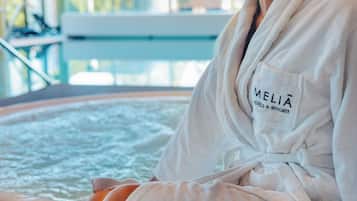 A person sitting in a bathtub with a towel, wearing a robe with 'MELIA HOTELS & RESORTS' text.