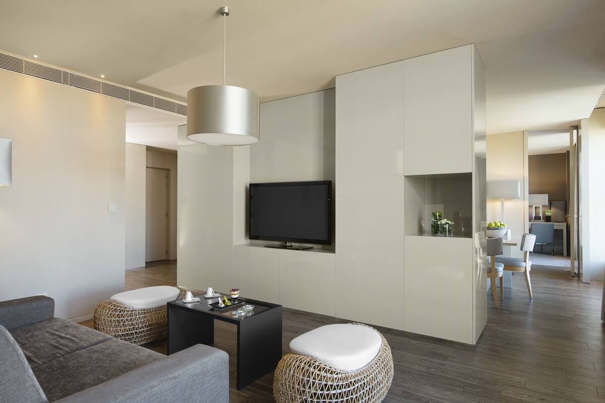 Een moderne woonkamer met een bank, poef, salontafel en een flatscreen televisie aan de muur.