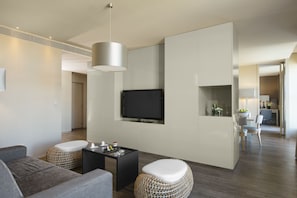 Un salon moderne comprenant un canapé, un pouf, une table basse et un téléviseur à écran plat fixé au mur.
