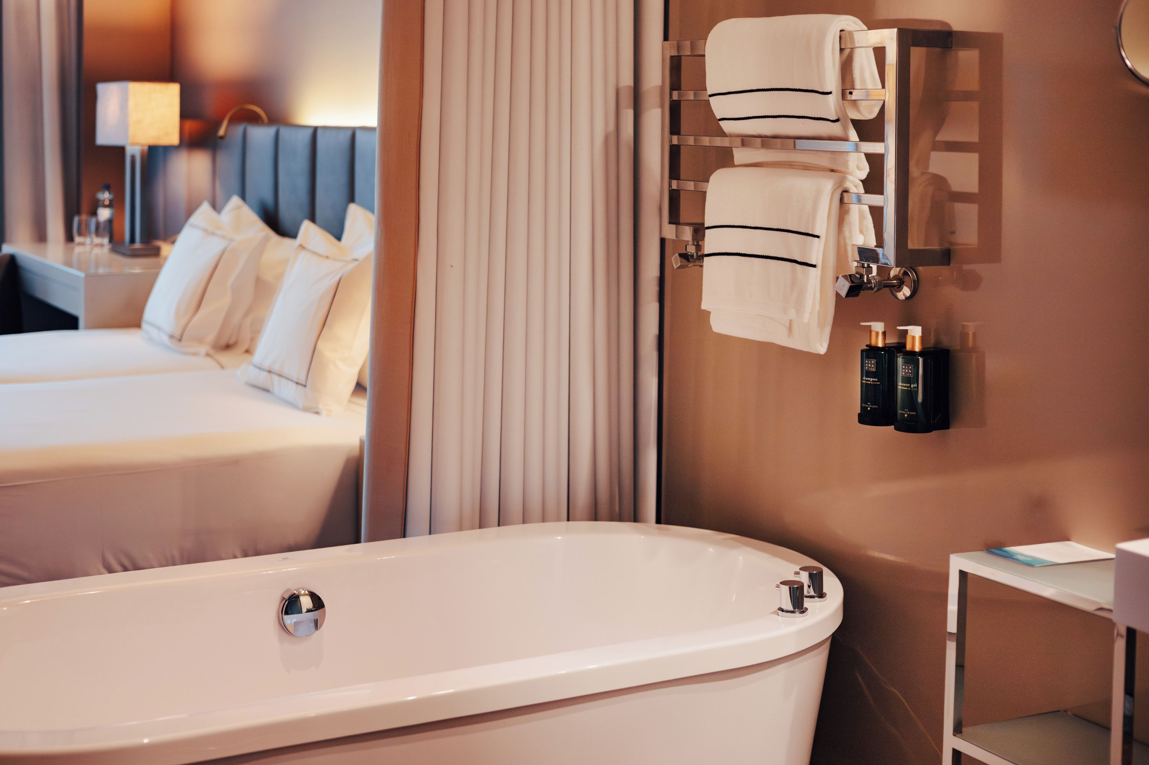 A modern bathroom with a freestanding bathtub, a towel rack with neatly folded towels, and a small shelf with toiletries.