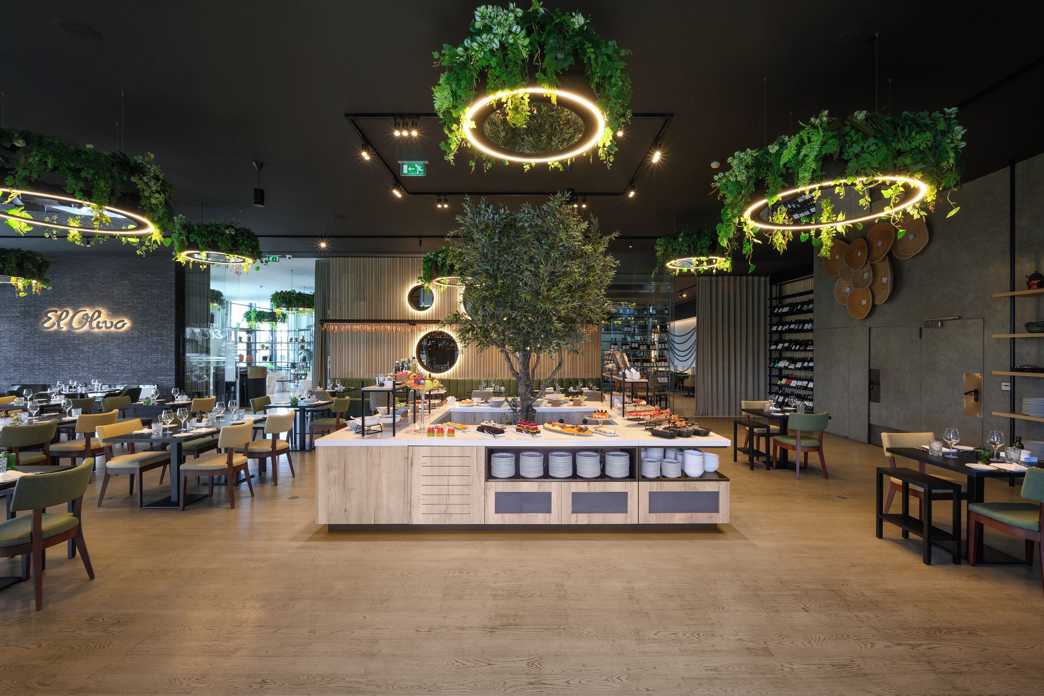 Un restaurante con una isla central, varias zonas de estar y una variedad de plantas y luminarias.